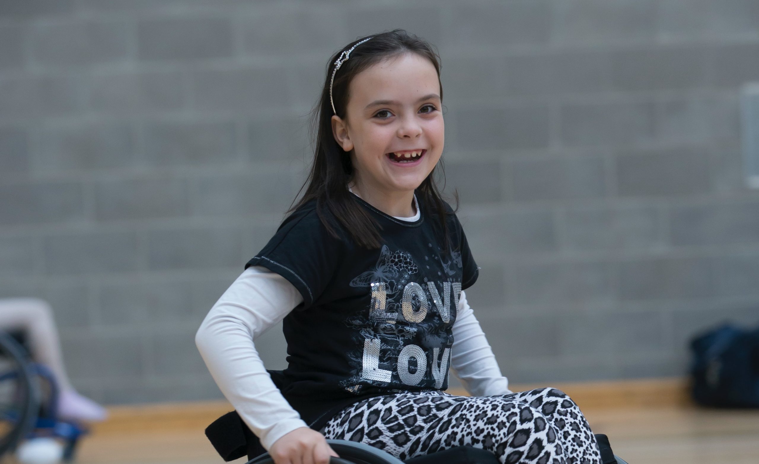 young girl in a wheelchair smiling in a gymnasium