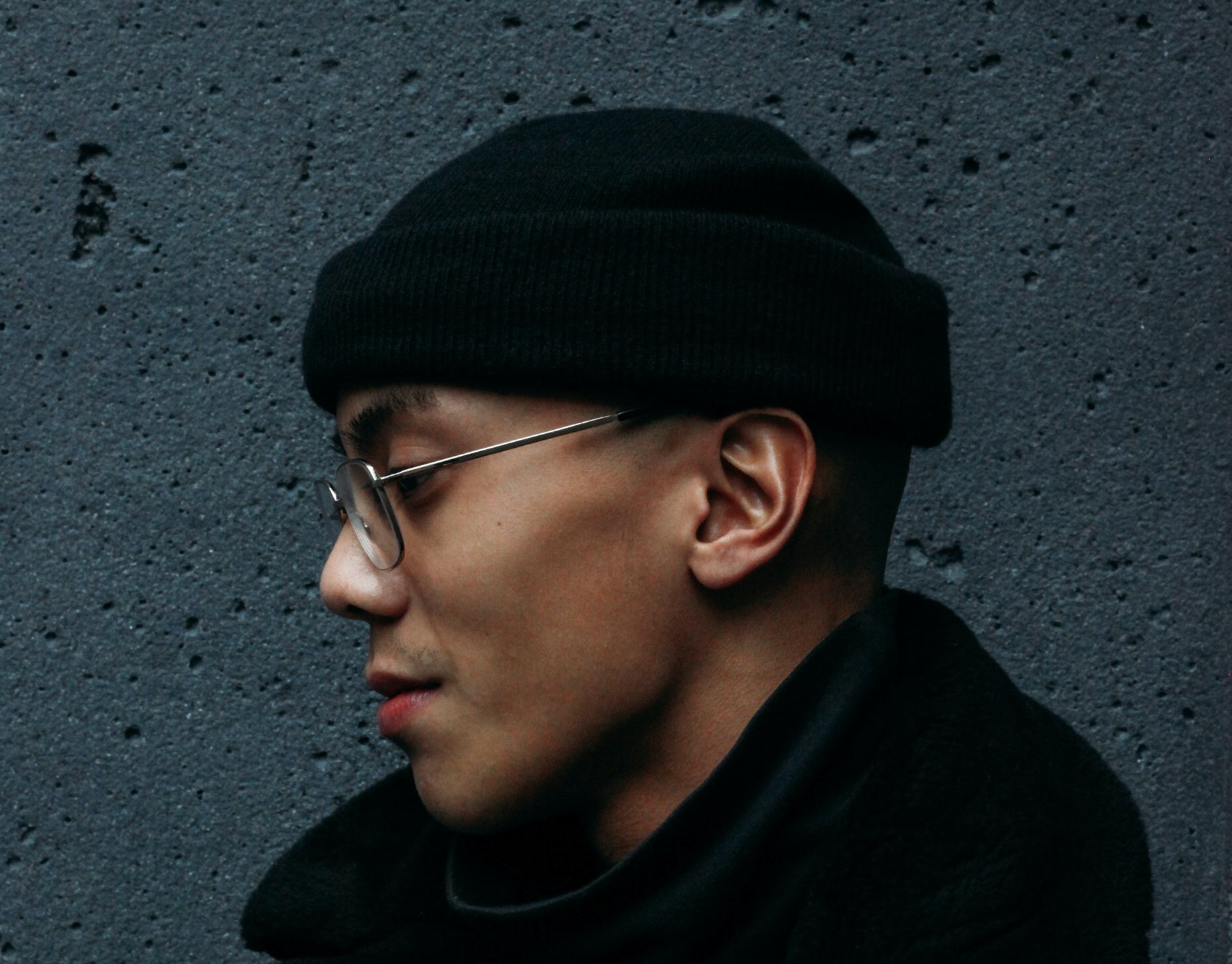 person with hat and glasses looking away standing by a wall