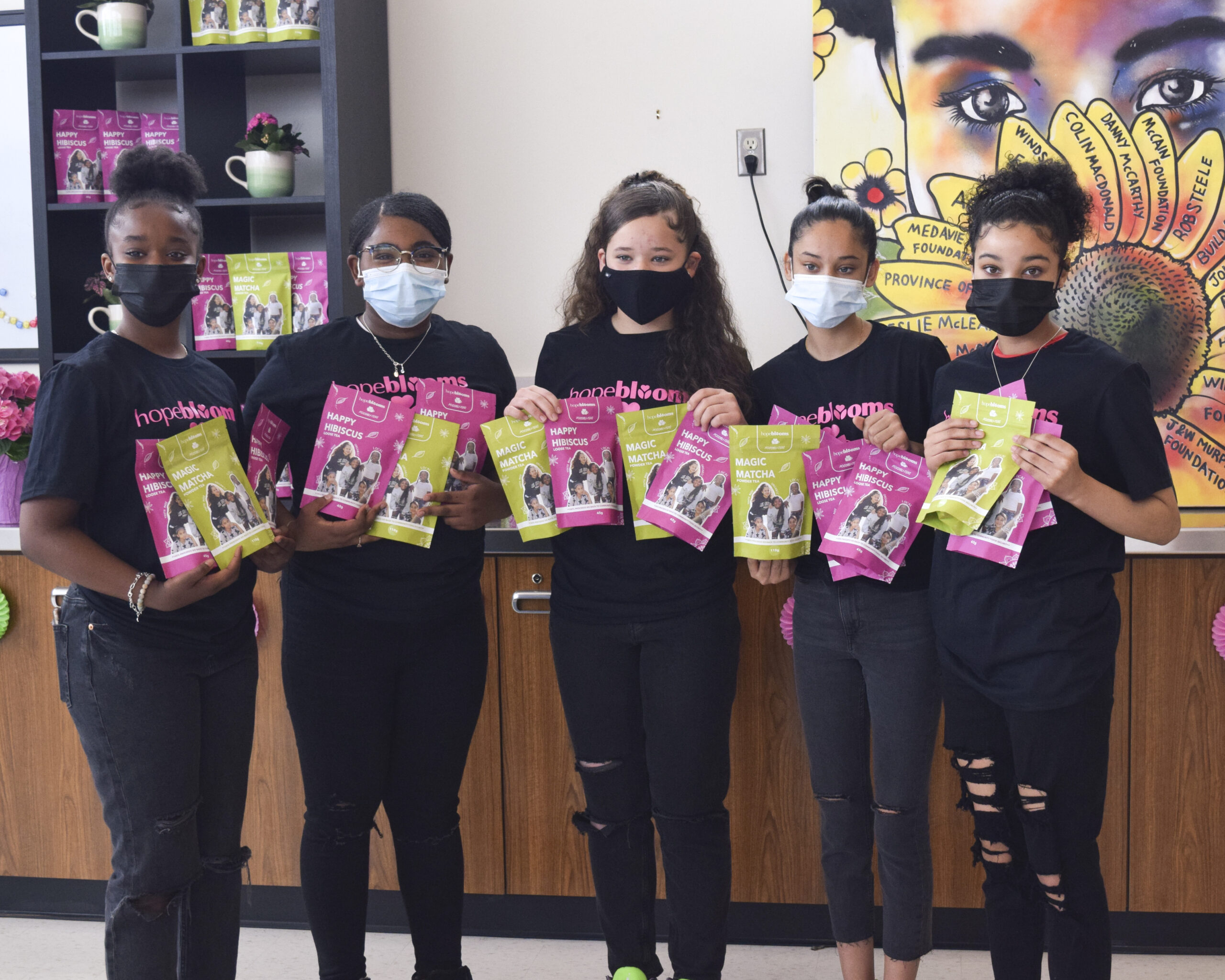 Five youth standing in a row holding brightly coloured packages of loose leaf tea
