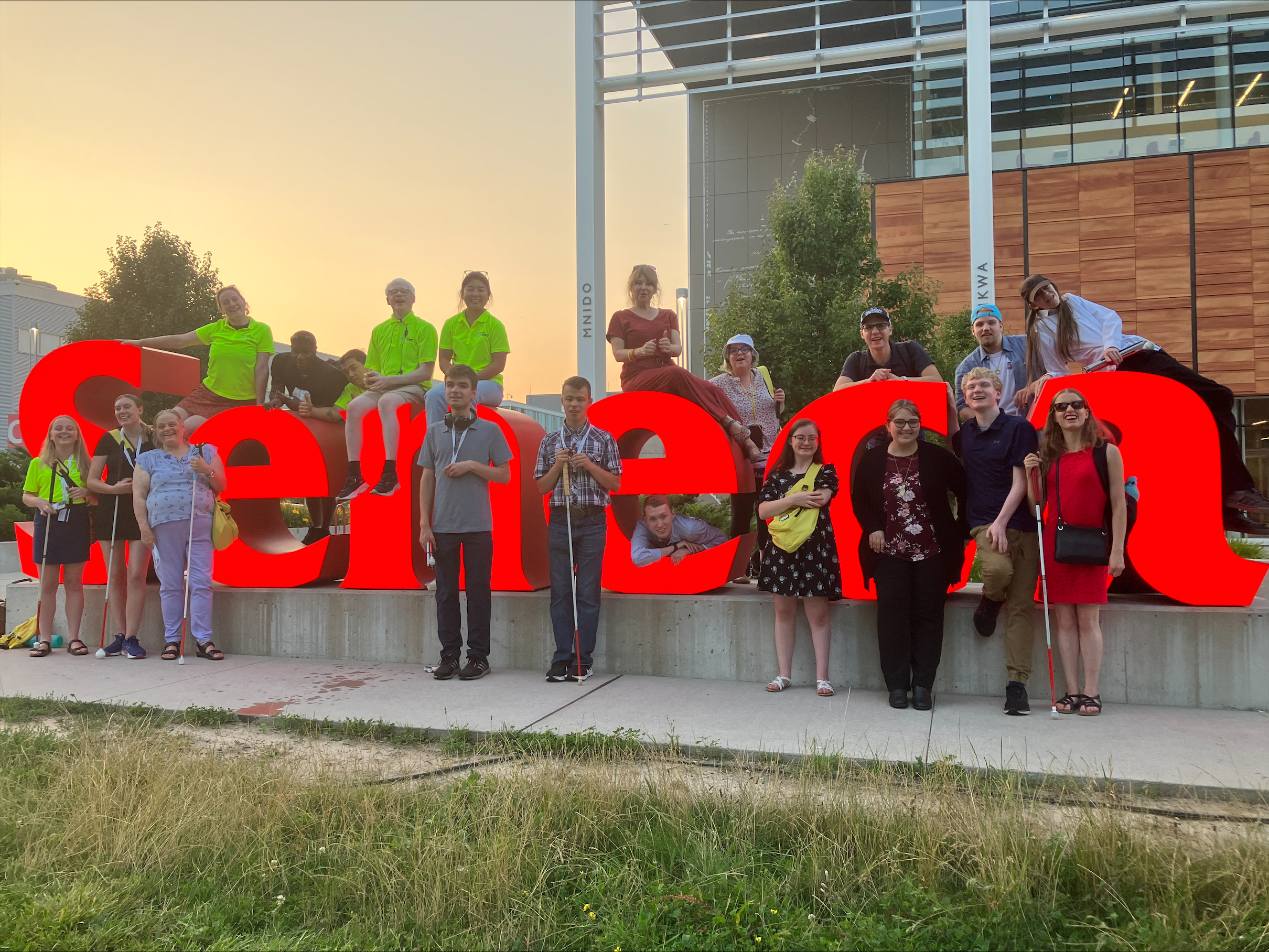 A group of people impacted by blindness pose with a glowing red sign reading "Seneca".