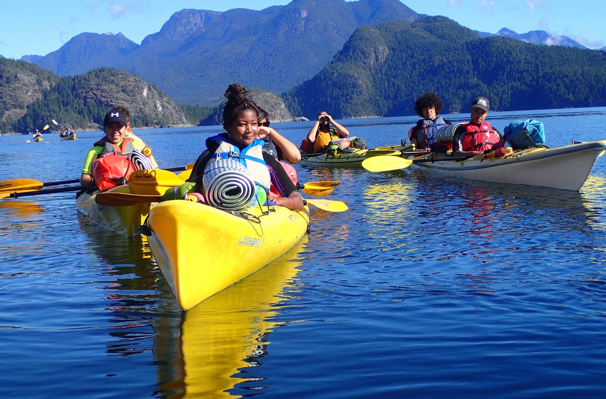 A group of young people kayaking on a lake.